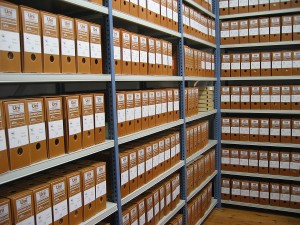 Shelved record boxes at an archive. Image courtesy of Depósito del Archivo de la Fundación Sierra-Pambley, through Wikimedia Commons.