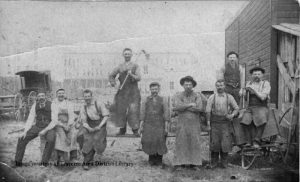 Victor Petertyl Wagon Works employees at the factory on State Street, 1891. (Note the Hannah Lay store on Front street in the background with almost nothing between them.) L-R: Vic Petertyl, Jim ? (woodworker), Wm. Abbott (horse shoer), Herman Koch (finisher), Albert Petertyl (blacksmith), Vencil Sleder (woodworker), Pat Robertson (helper and horse shoer), Chas. Weland (painter) and Anton Petertyl. (At the far left is either the Union Street Hotel or the back of the Masonic Building. Opinions vary.) Perhaps a member of the Sleder family can inform us the relationship between Vencil and Vaclav. From the Photo Collection at Traverse Area District Library Local History, 718.000001.100.